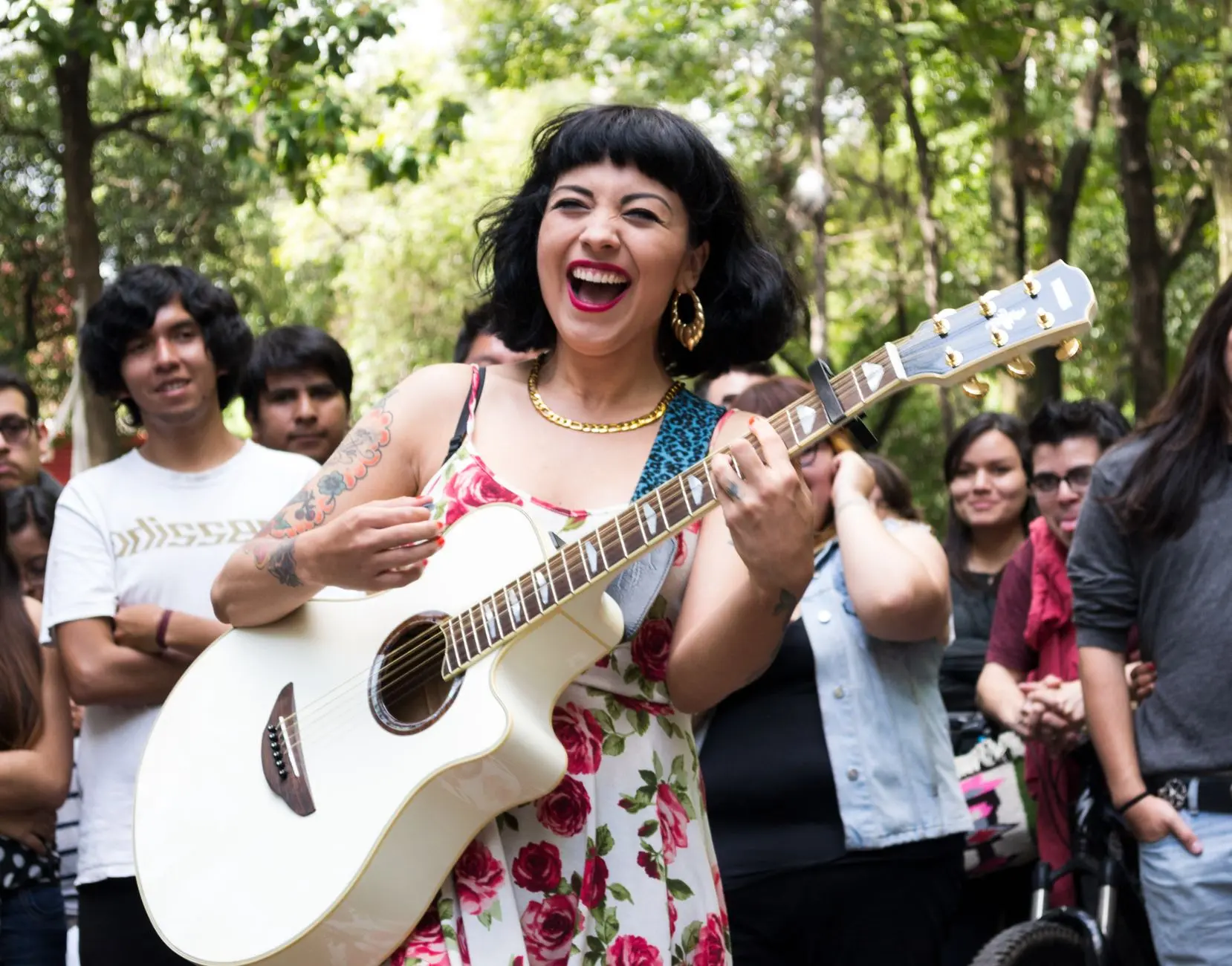10 ganadores históricos del Latin Grammy 12 Mujer tocando la guitarra con una multitud animada en un entorno vibrante de calle.